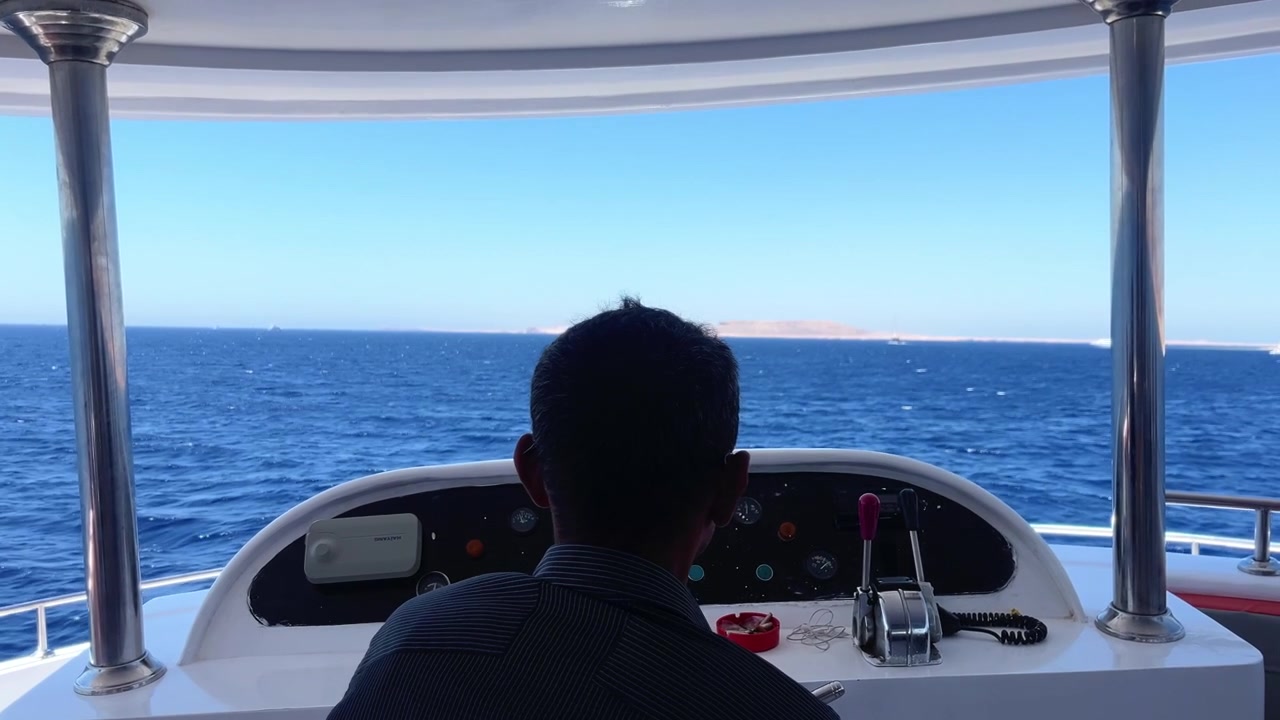 Person steering a boat across deep blue sea with distant coastline in Egypt