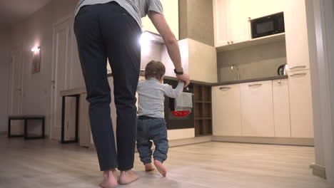 rear view of a father helping his son take his first steps