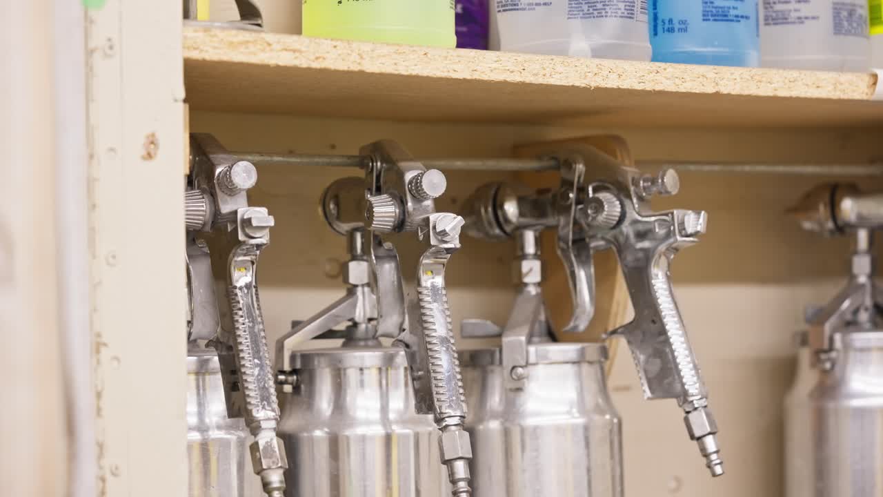 Pan across chrome spray guns hanging on wall inside an industrial workshop