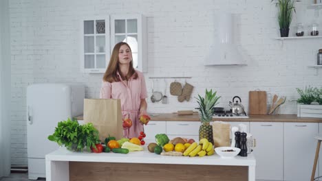 healthy food on a kitchen table. beautiful woman taking out fresh apples from shopping bag. loving mom cares about nutrition.