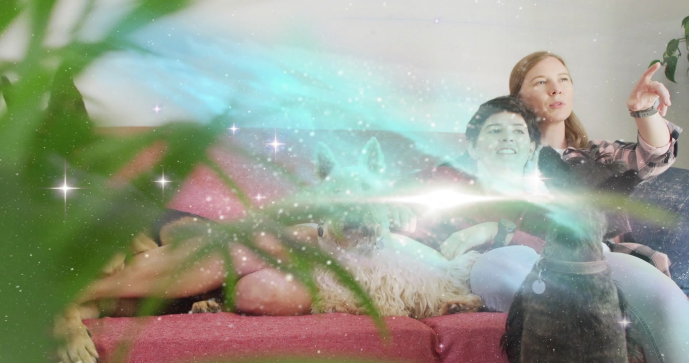 Two women sitting on pink sofa leaning, teal sparkles sweeping right revealing dogs for marketing