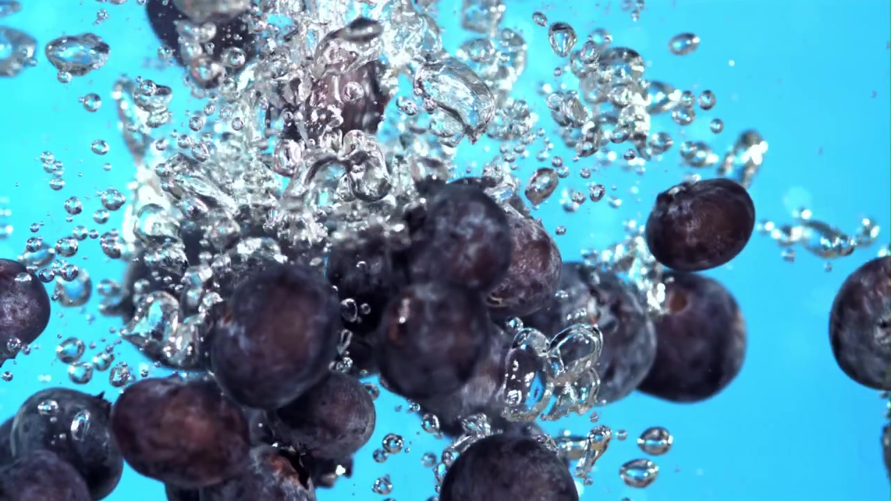 Färska blåbär som faller ner i vatten med bubblor i slow motion
