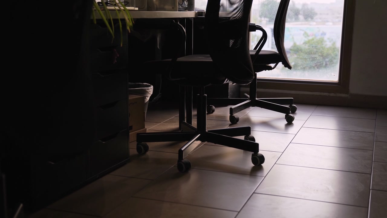 Cinematic low angle shot of an empty modern office workspace with black mesh chairs and natural daylight through a large window. Ideal for corporate background b-roll.