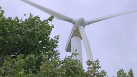 Wind-turbine-turning-oblique-view-with-swaying-trees-on-windy-and-cloudy-summer-day