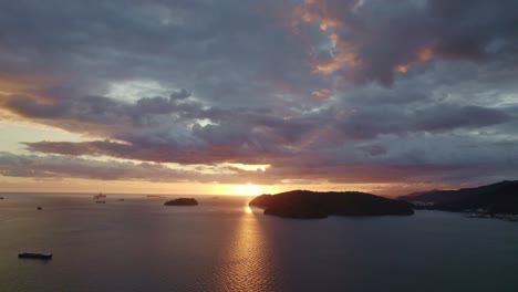 drone shot of sunset behind mountains on the ocean with dramatic clouds and reflection in the water