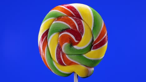 rotation of a spiral fruit lollipop on a blue background. caramel lollipops. sweets for children.macro.childhood concept.