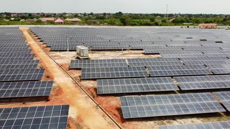 Luftaufnahme-Eines-Solarparks-Mit-Drohne,-Die-In-Richtung-Eines-Industriellen-Wechselrichters-In-Jambur,-Gambia-Fliegt