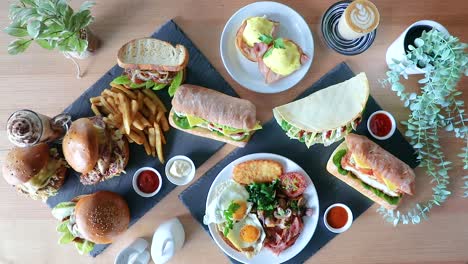 cafe latte pushed into frame next to brunch flat lay with sandwiches, burger and chips