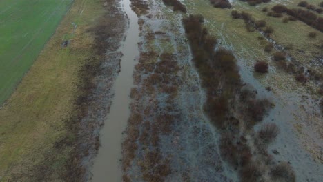 aerial establishing view of high water in springtime, alande river flood, brown and muddy water, agricultural fields under the water, overcast day, wide drone shot moving forward tilt up