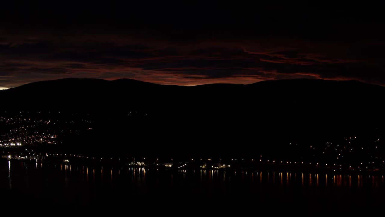 закат в новой зеландии в горах с далеким горно-городским светом и красным небом