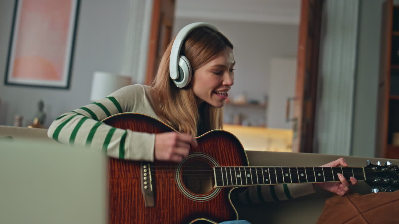 Girl musician enjoy guitar sound wearing headphones at home couch close up.
