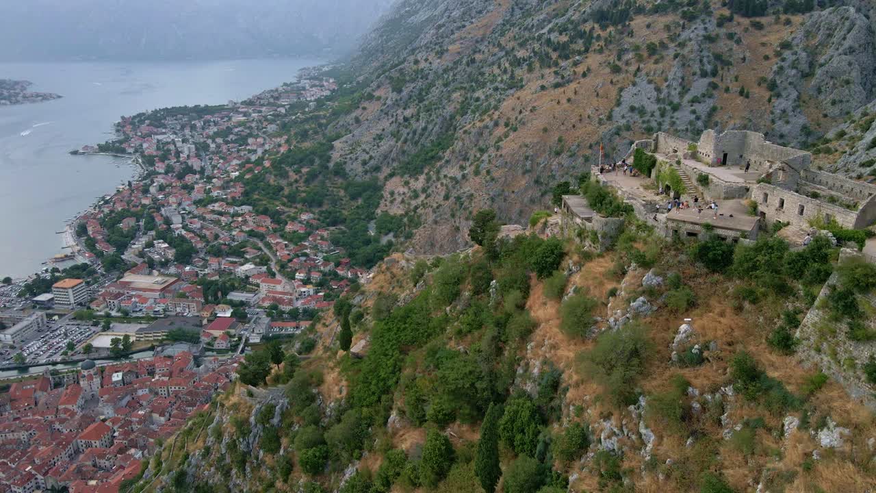 Karadağ, Kotor'da, San Giovanni Kalesi Harabeleri'nin üzerinden çekilmiş dramatik bir hava görüntüsüyle soldan sağa doğru ortaya çıkan eski şehir ve lüks yat limanı.