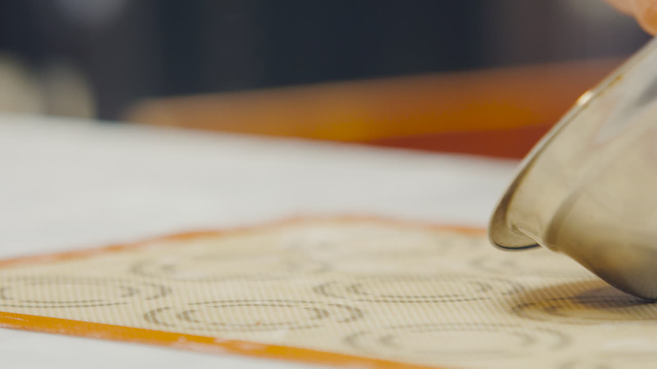Hand spreading dough with a spatula on a baking mat
