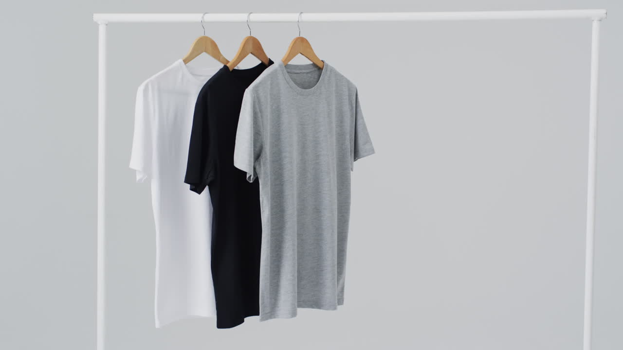 Video of white, grey, black t shirts on hangers and copy space on white background