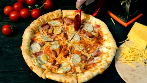 las manos cortadas de la pizza, en rebanadas, con salchichas, tomate y queso, con un cuchillo especial.