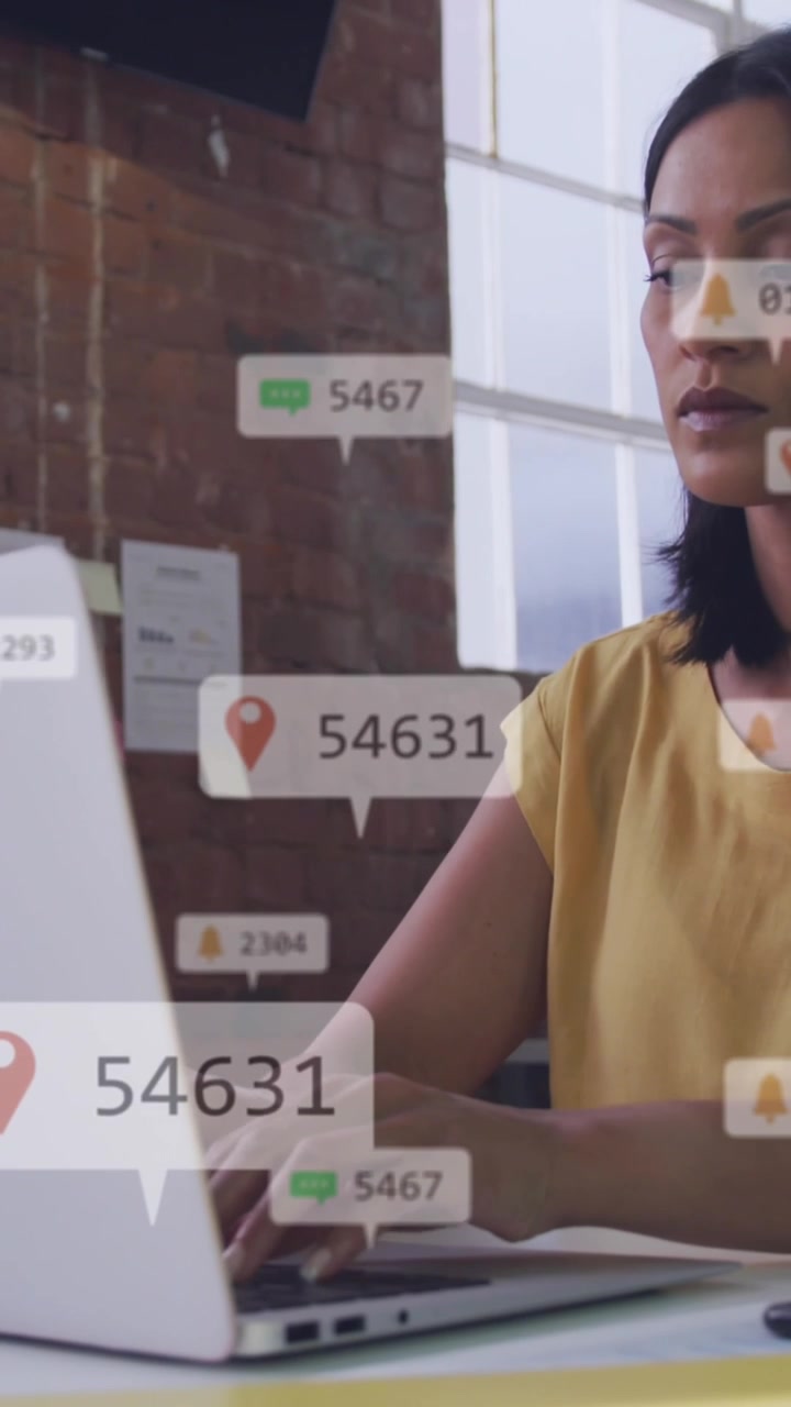 Animation of social media icons floating against woman using a laptop at office