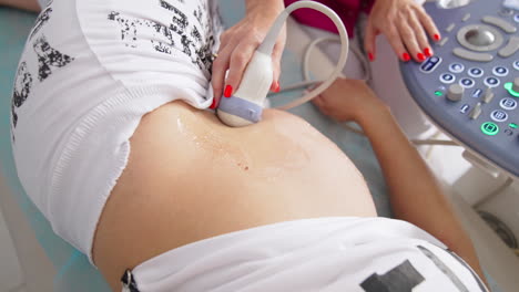making ultrasound of baby in clinic office. pregnant woman laying on bed during ultrasound. doctor gynecologist performing screening belly of pregnant woman. top view.