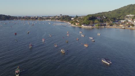 Aerial view from sea towards anchored wooden fishing boats, coastal houses, and green hills during afternoon