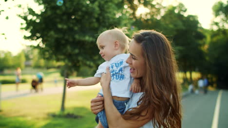 Woman-and-boy-standing-in-park.-Mother-and-son-playing-with-soap-bubbles