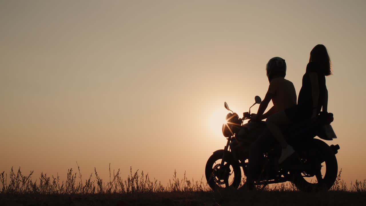 una pareja joven se sienta en una motocicleta juntos admirando la puesta de sol