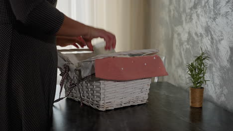close up of young adult in plaid clothing dropping white basket filled with different items onto dark marble table carefully removing each item and placing on table cozy kitchen
