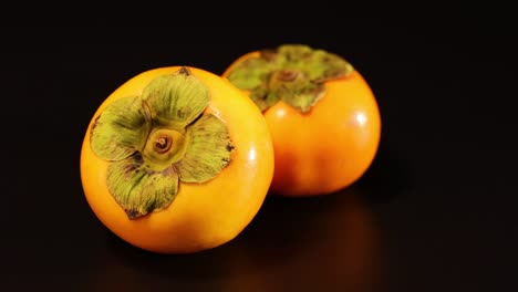 two persimmons resting on a dark background