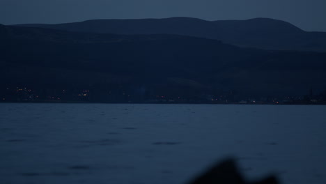 coastal town lights twinkle in distance at base of mountains across water