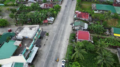 Aerial-Drone-Flyover-of-Tropical-Village-Neighborhood-Street-with-tricycles-and-mopeds-driving