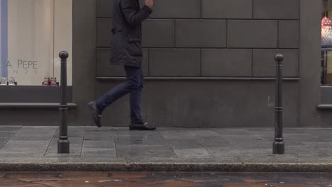 Slow-motion-shot-of-a-guy-walking-fast-in-the-rain-in-Milan-due-to-rainy-weather