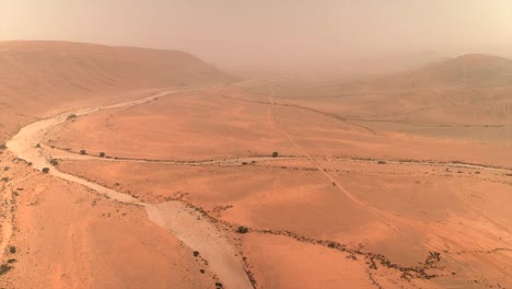 aerial view of dry, sandy riverbed (wadi) winding through the vast desert landscape under a hazy sky near tan-tan, morocco