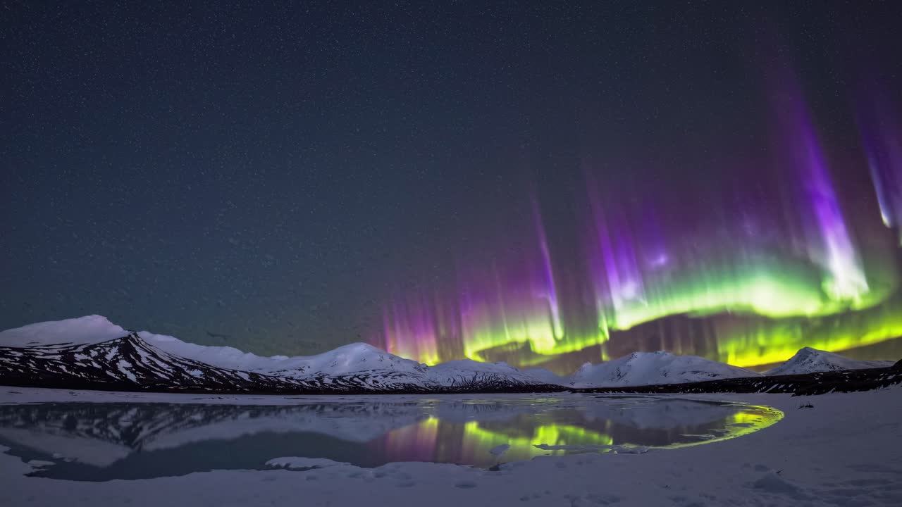 Wide-angle video captures serene snowy mountains and vibrant aurora borealis reflected in a calm