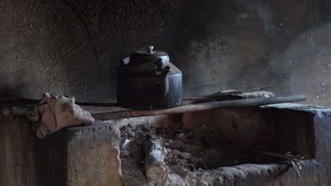 rustic iron kettle resting over traditional open fire pit indoors in rural village