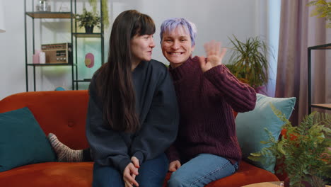 lesbian women family smiling friendly, waving hands gesturing hello, hi, greeting at home on couch