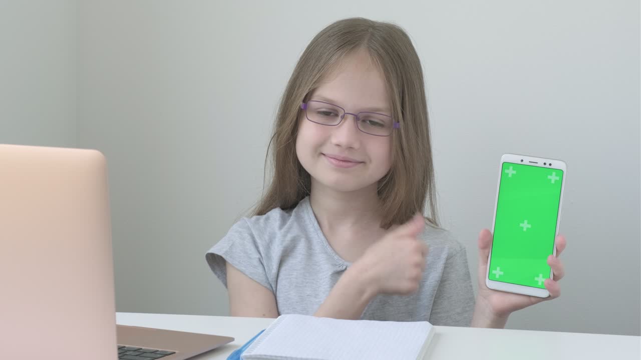 Schoolgirl in glasses shows phone with green screen mock up cellphone, mobile telephone