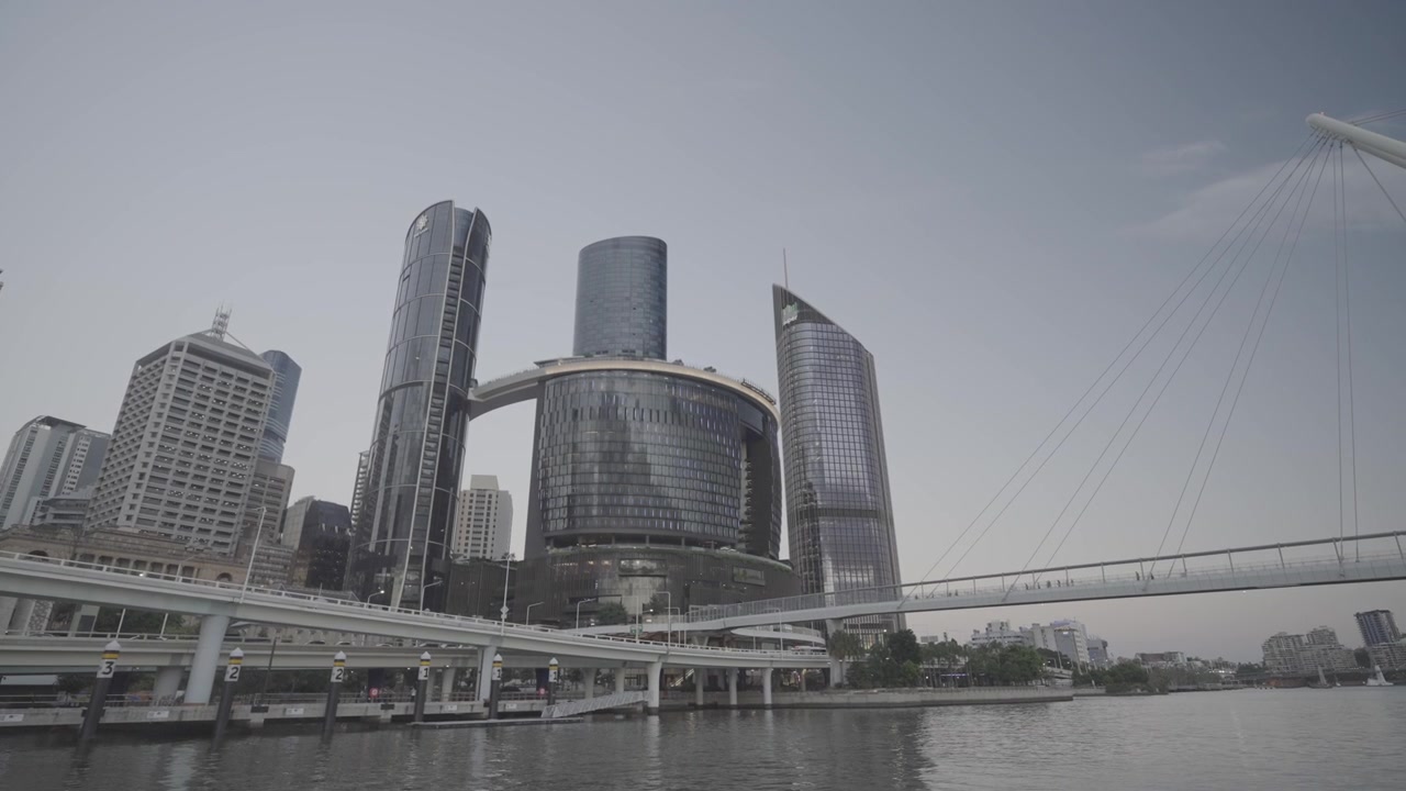 Modern high rise towers rise along the Brisbane riverside skyline beneath a soft dusk sky. The Star Casino and Nevill Bonner Bridge are both visible.