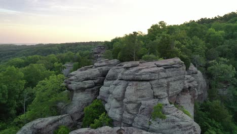 Majestic-stone-cliff-surrounded-by-vast-forest-landscape,-aerial-view