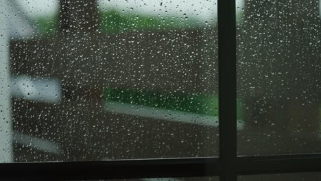 Raindrops-slowly-rolling-down-window-as-heavy-storm-winds-blow-outside-in-Stuttgart,-Germany,-Baden-Wurttemberg-Europe,-panning-view-angle