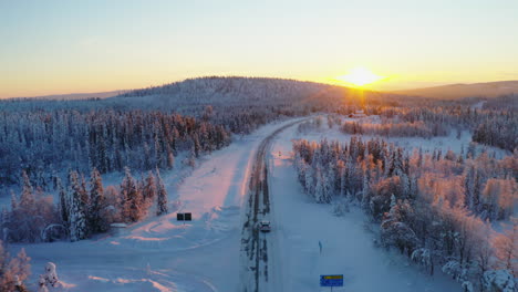 aerial view above vehicle joining snowy remote road heading towards woodland mountain sunrise