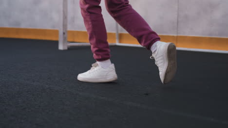 leg view of female athlete jogging around curved barbed wire sports court under soft dusk sky, white sneakers stepping on smooth asphalt beside yellow edged barrier wall and chain link fence panel