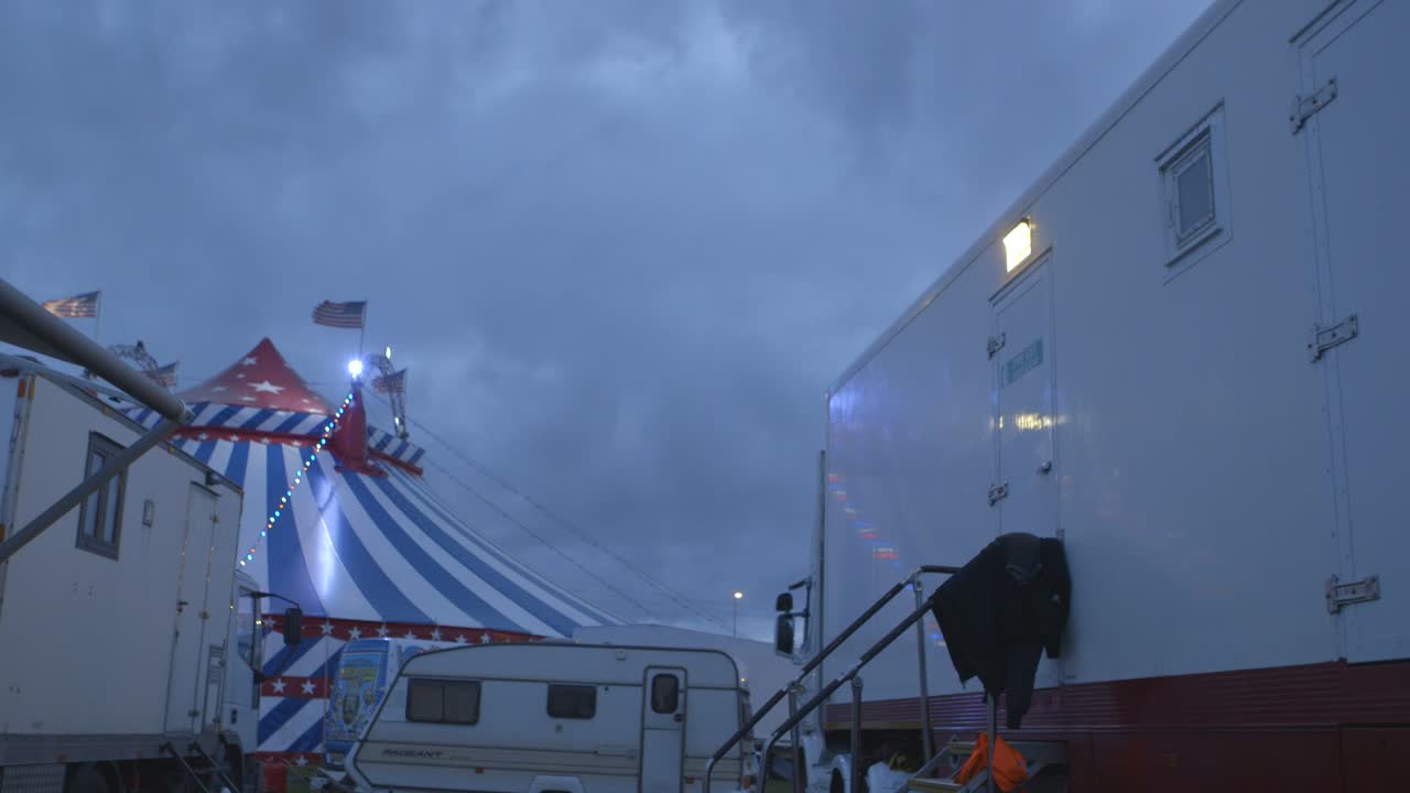 Cirkusartistvogn i forgrunden med cirkustelt i baggrunden om natten