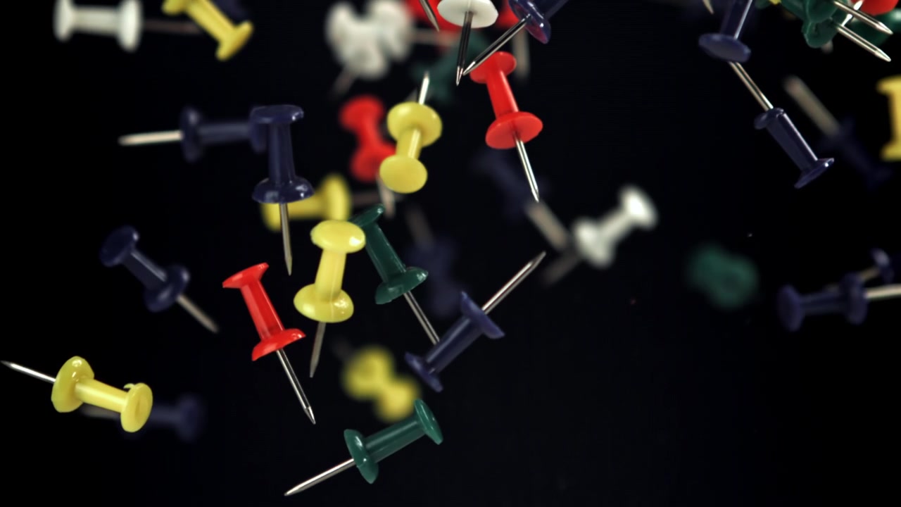 Colorful Pushpins Falling in Slow Motion Against Black Background