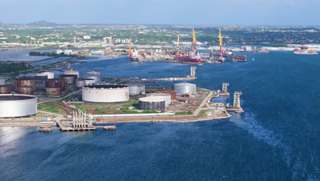 aerial parallax around oil refinery stack and storage vats on coast of tropical island