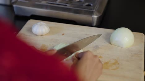 Young-skinny-brown-woman-dicing-white-onion-with-chef's-knife-on-cutting-board