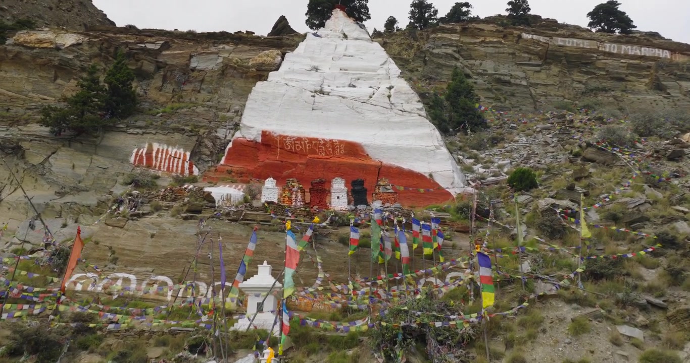 Landsbyen Marpha, Nepal, droneopptak i bane av en tradisjonell hvit og rød buddhistisk chorten bygget inn i en robust, steinete fjellside prydet med bønneflagg.