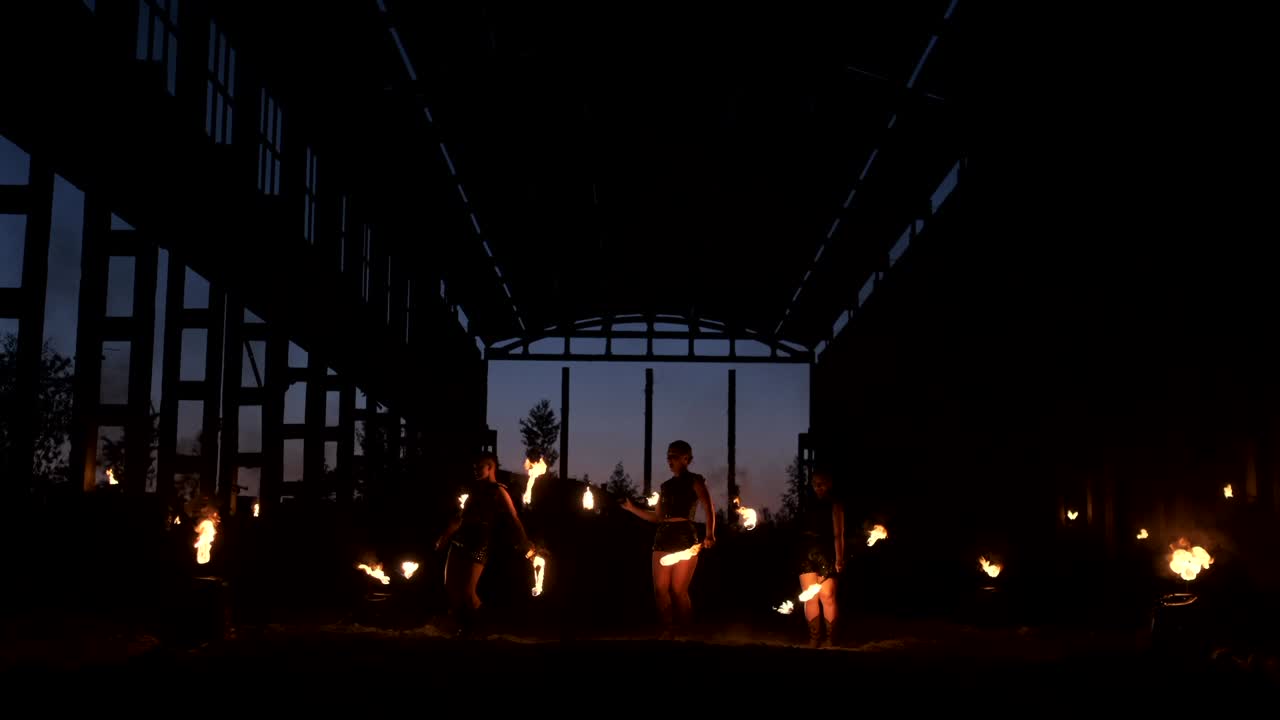 A group of people with fire and torches dancing at sunset in the hangar in slow motion. Fire show