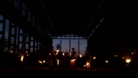a group of people with fire and torches dancing at sunset in the hangar in slow motion. fire show