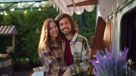 Portrait:-Happy-brunette-guy-with-his-girlfriend-in-a-plaid-shirt-hugging-and-talking-while-standing-Near-his-trailer-during-a-picnic-in-a-camp-outside-the-city-in-the-summer