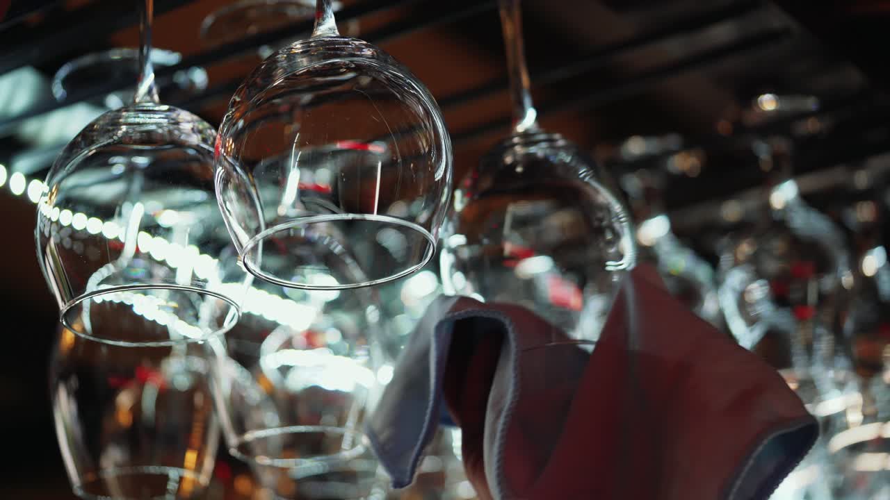 Clean wine glasses hanging upside down above a bar rack in restaurant. Bartender wipes glasses