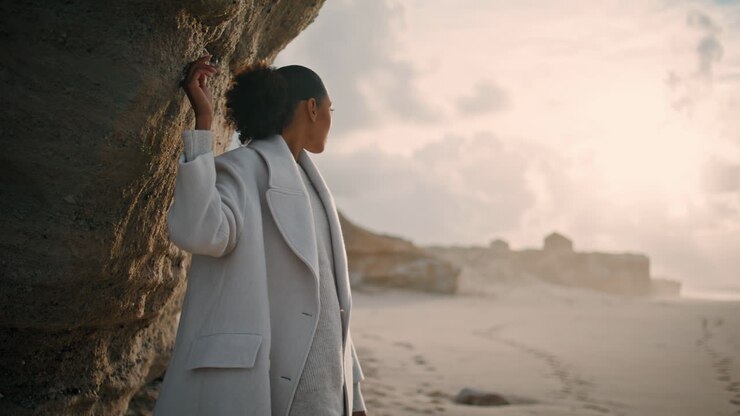 Beautiful girl touching cliff wall on empty beach. Serene african american enjoy
