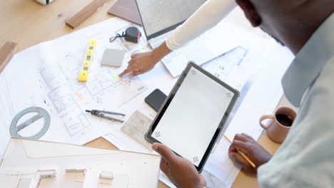 Using tablet and discussing blueprints, business colleagues collaborating in office